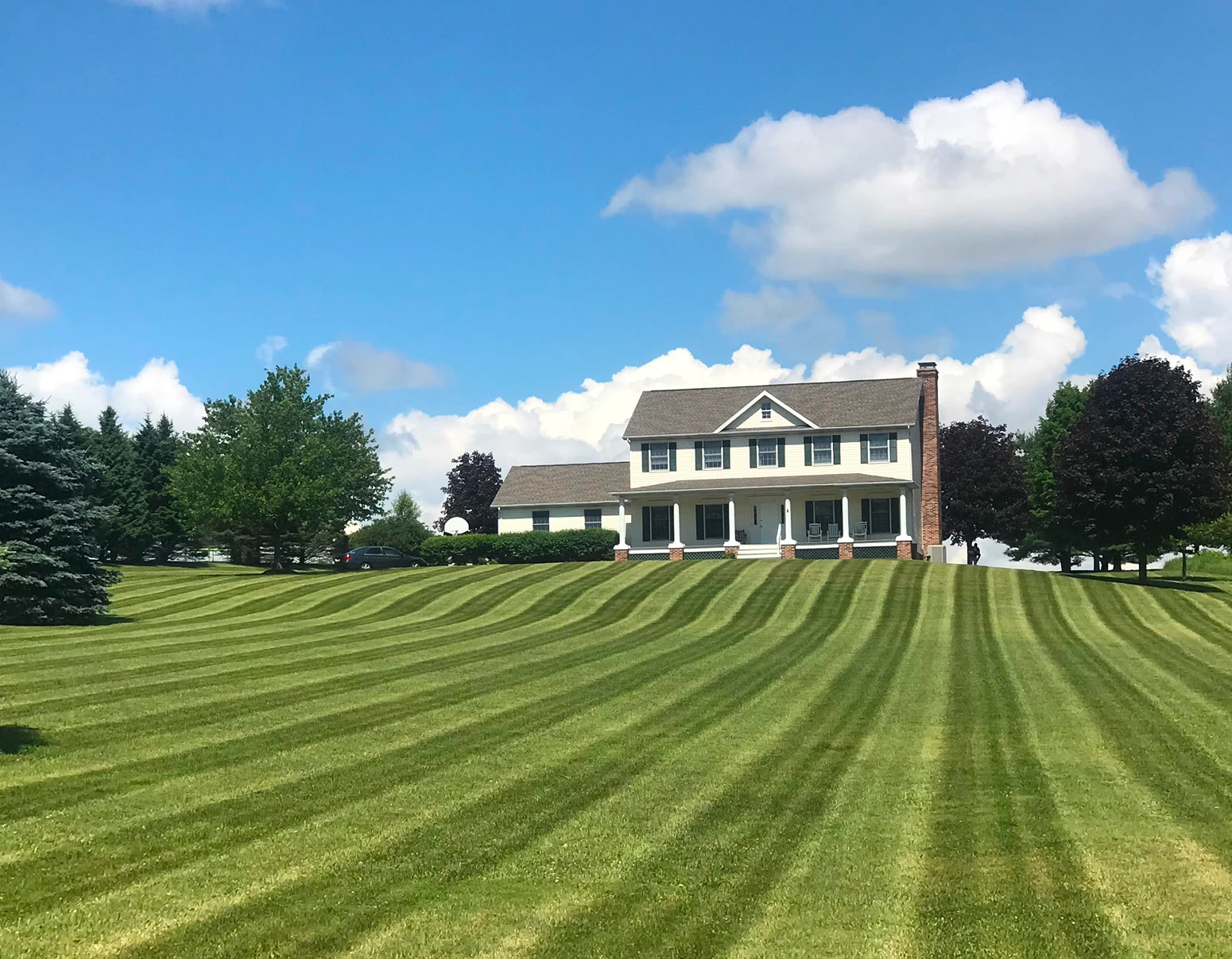 Large, elegant white estate house with a massive, perfectly striped green lawn in the foreground.