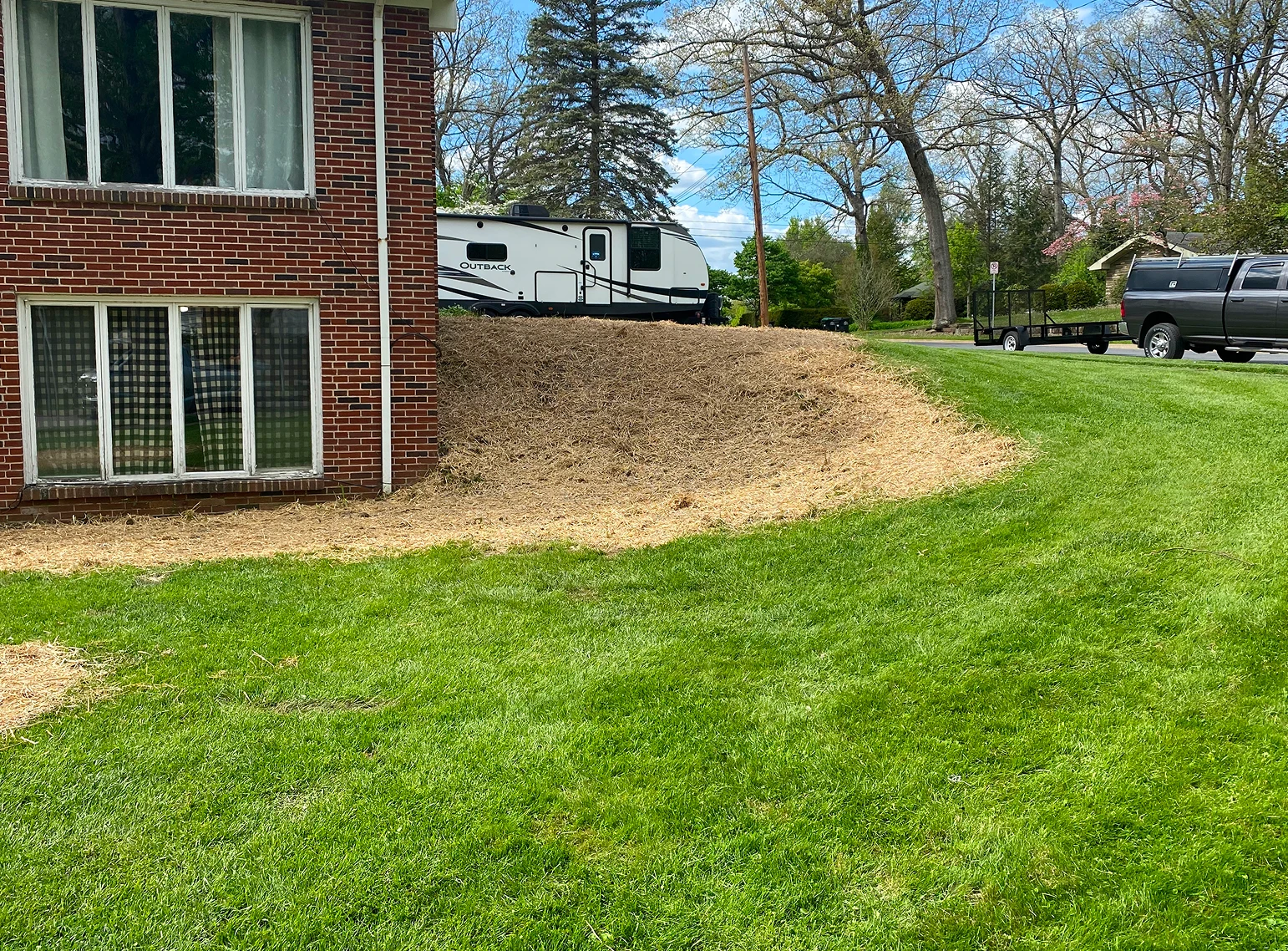 A freshly graded and seeded lawn slope next to a house with a camper trailer in the background.