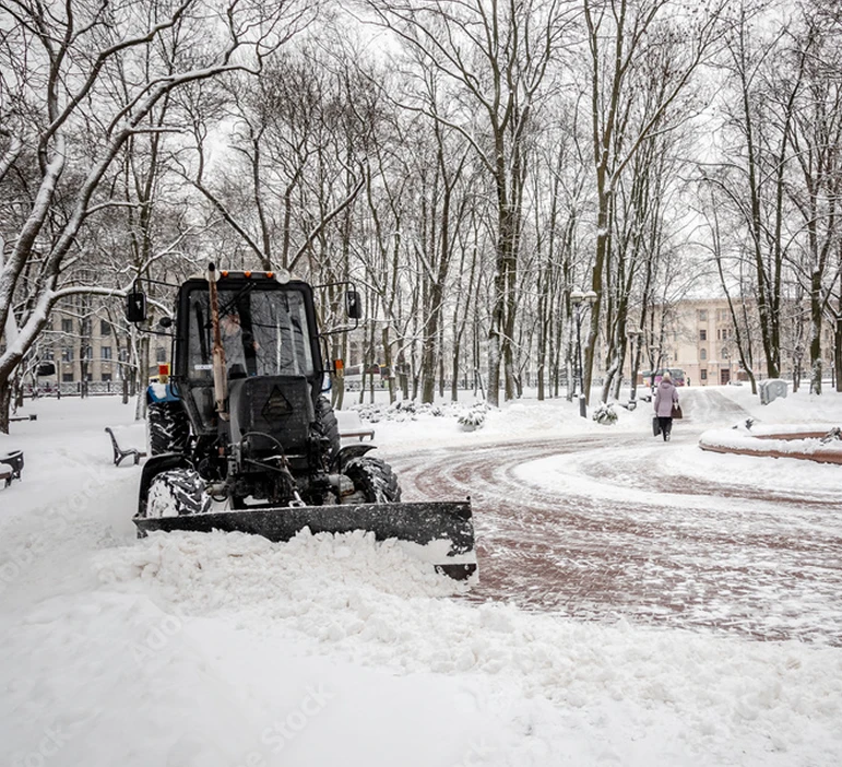 A specialized snow removal machine clearing a snow-covered parking lot or driveway in winter.