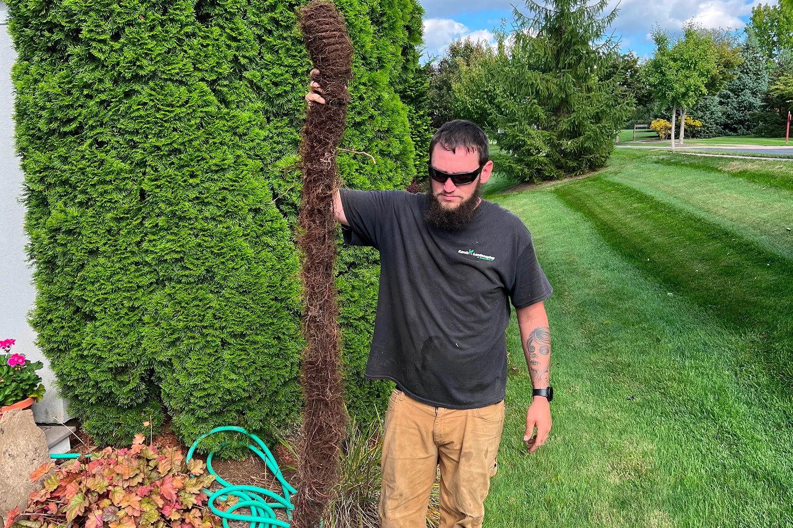 A man standing next to a tree trunk in a vibrant green backyard.
