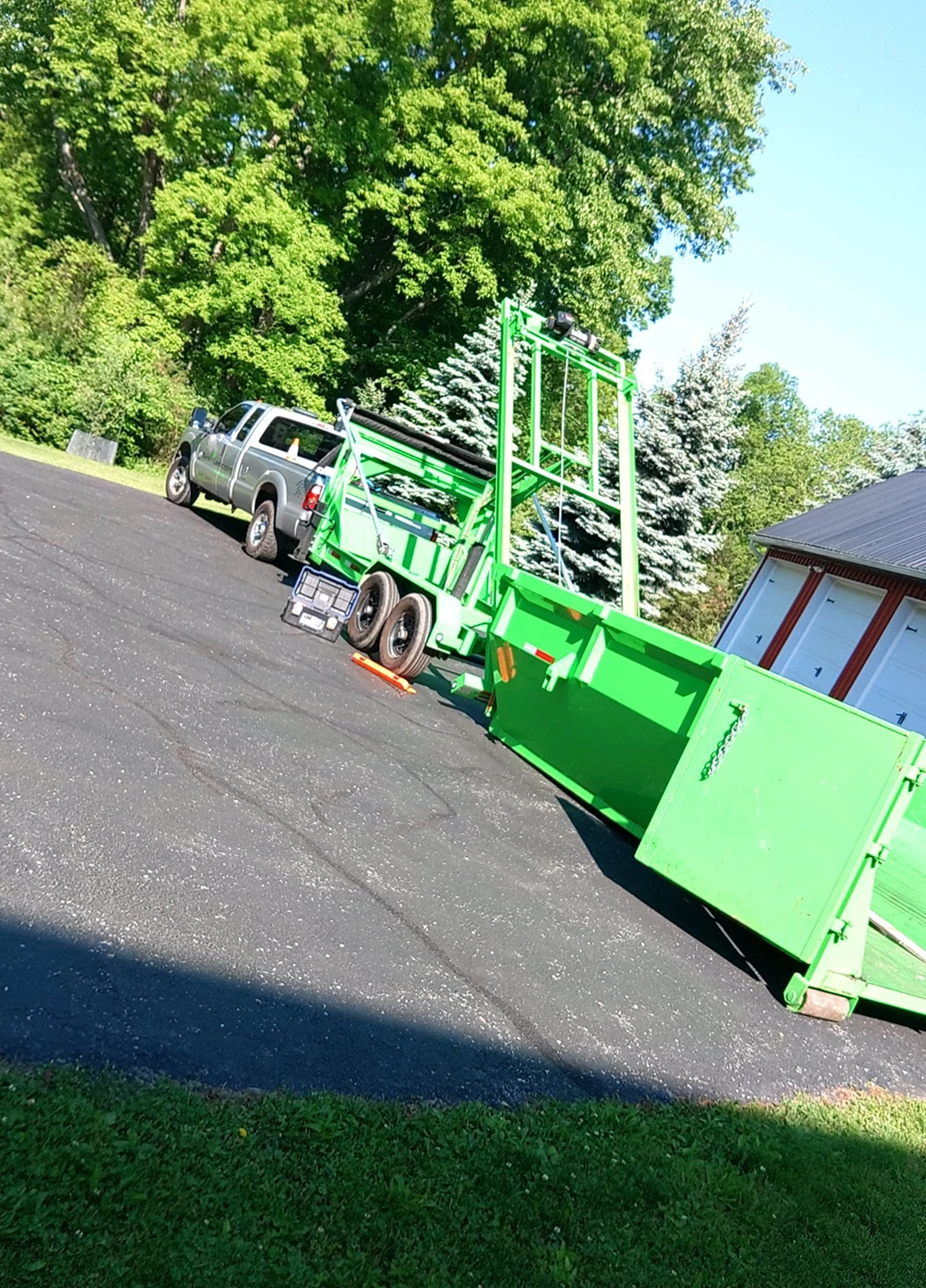 A bright green commercial dump trailer parked along an asphalt driveway.