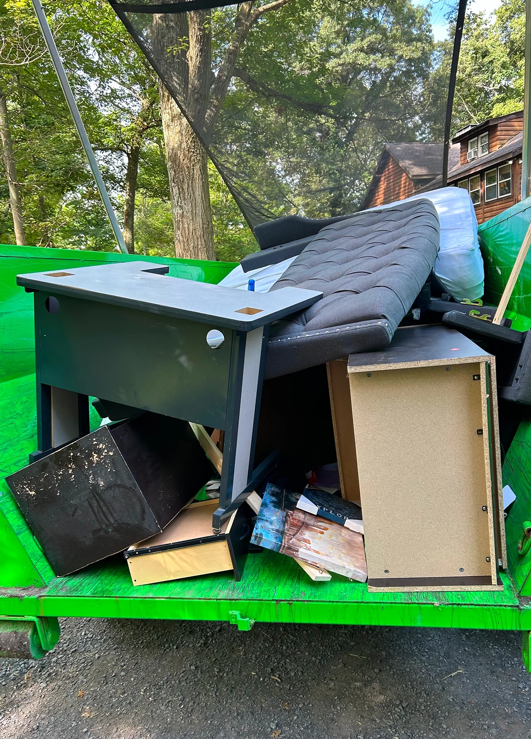 Back of trailer containing discarded furniture, including a desk and cushions.